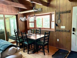 A wooden dining area with a table and chairs, a window with a view of greenery, and a coat rack with hangers.