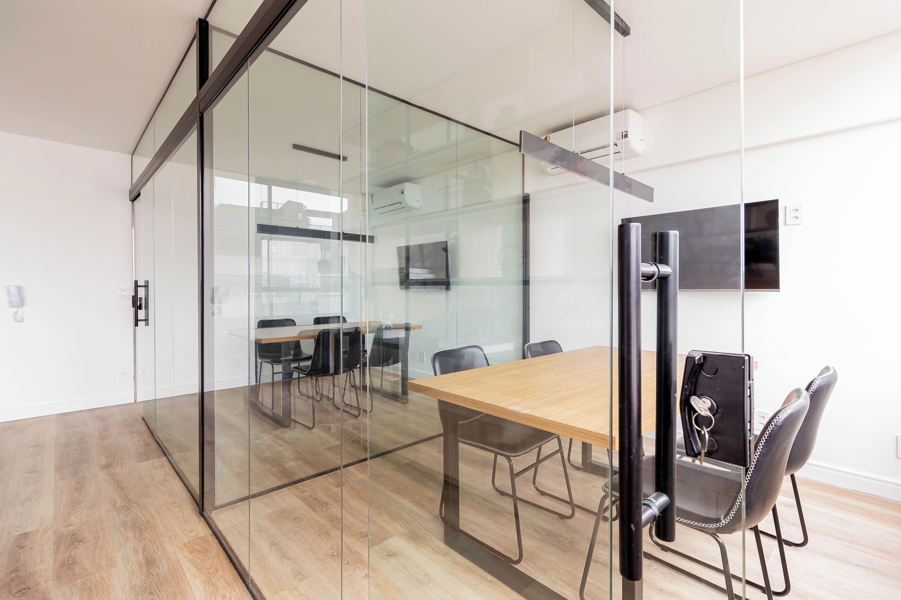 A modern conference room with glass walls, a wooden table, and black chairs.