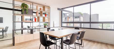 Una sala de reuniones moderna con una mesa grande, cuatro sillas, un divisor de vidrio y una estantería de madera con objetos decorativos.
