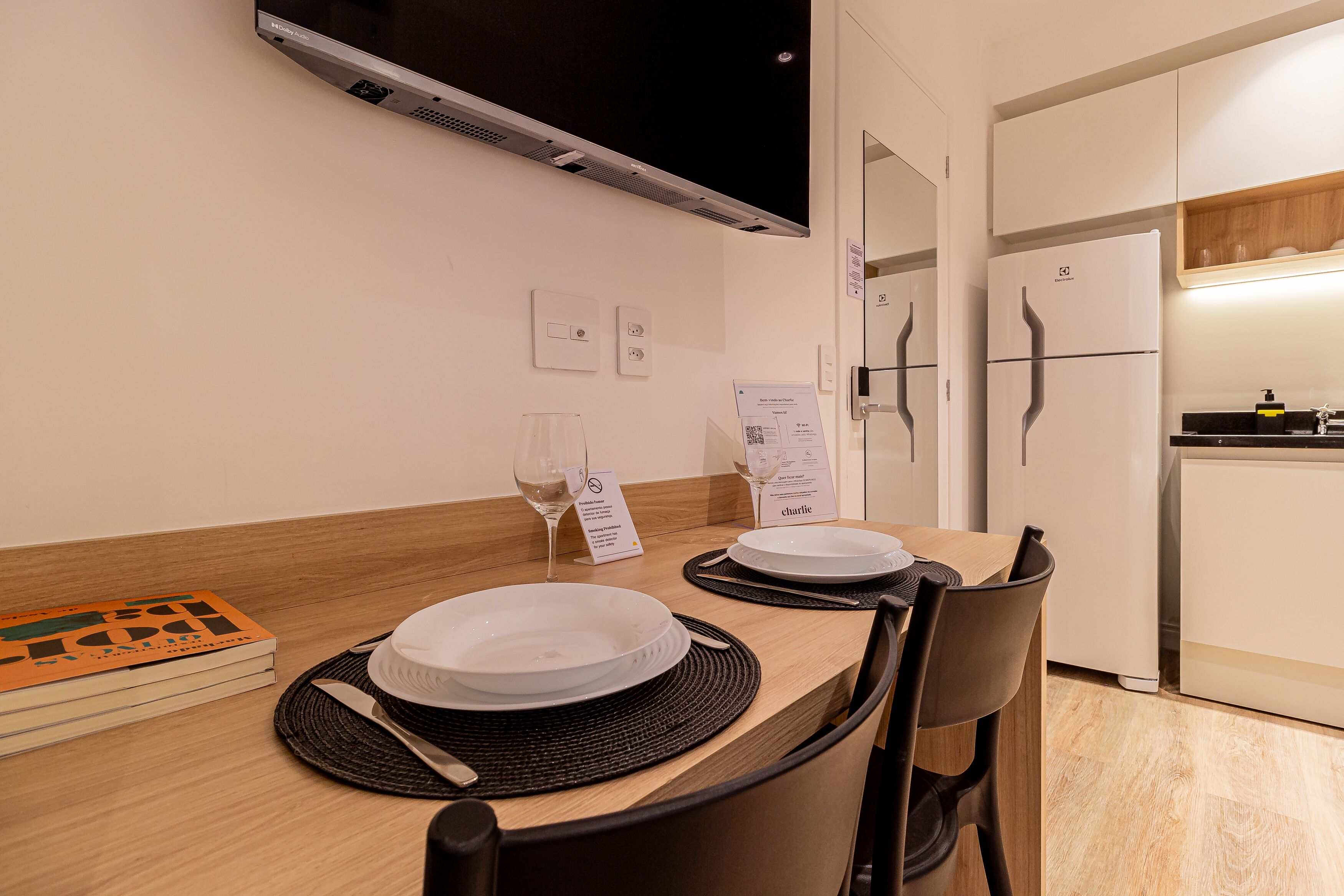 A dining area with a table set for two, a microwave, a refrigerator, and a wooden floor.