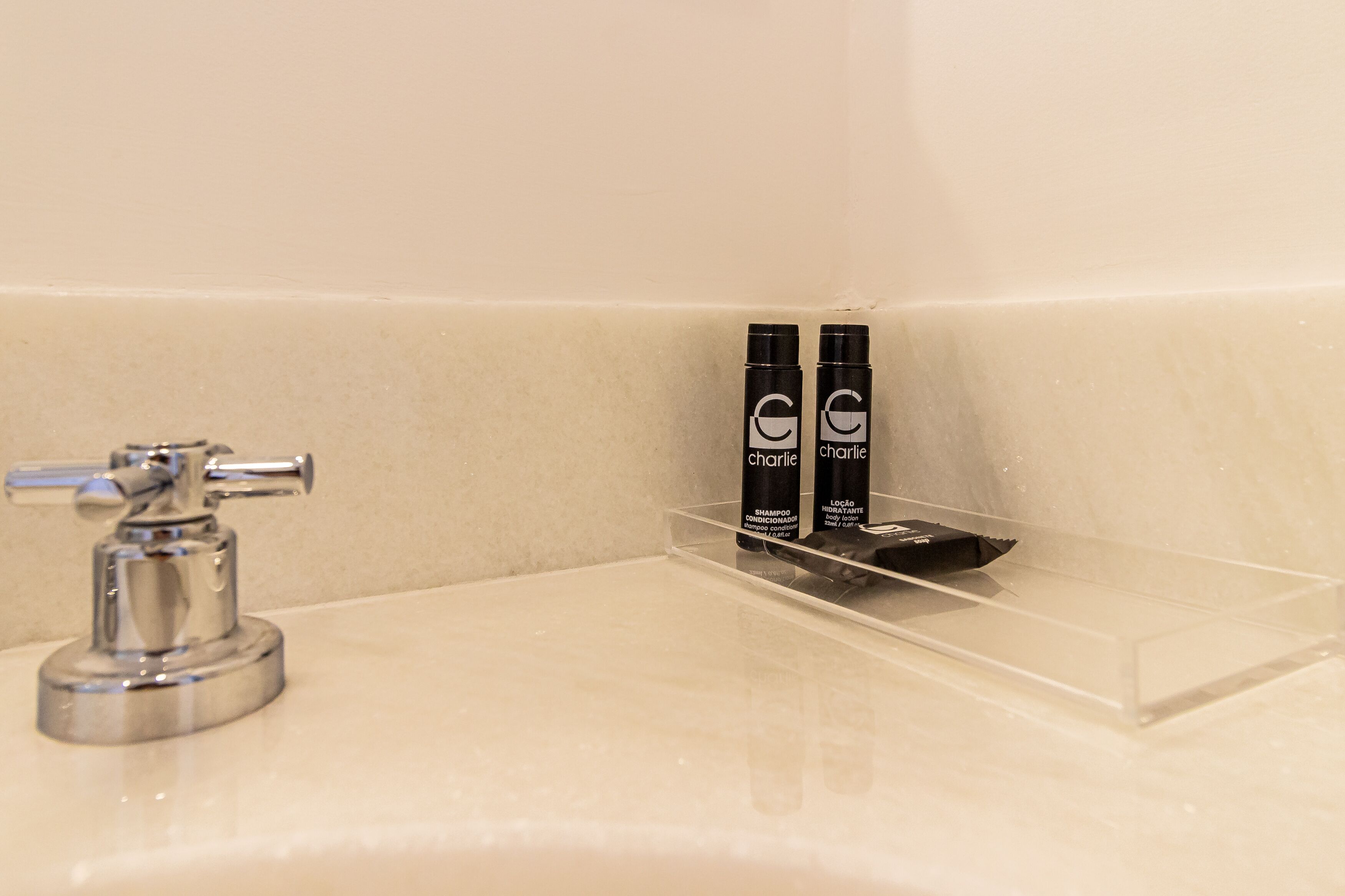 A bathroom with a chrome faucet and a clear shelf holding two bottles of shampoo.