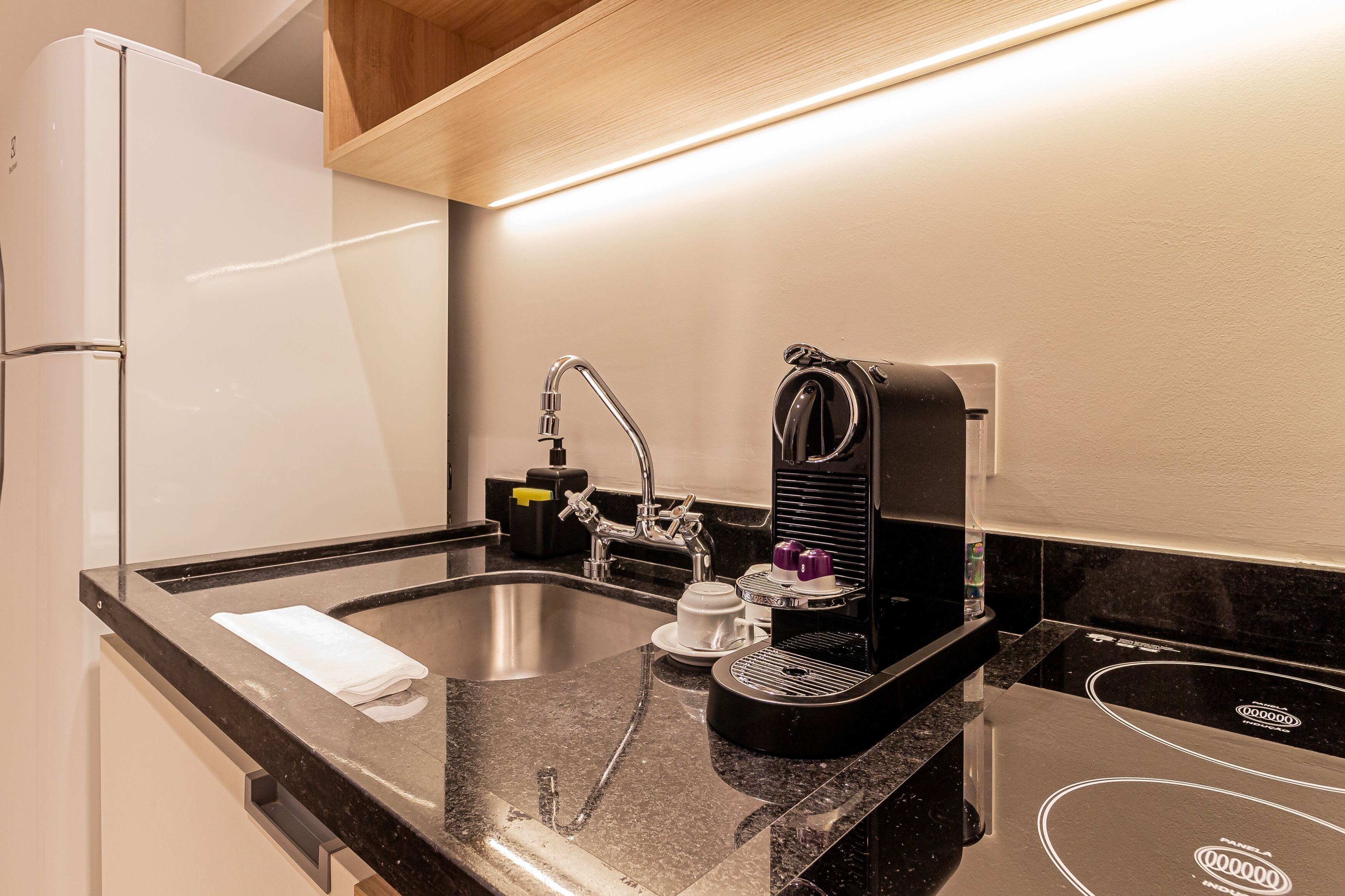 Una cocina moderna con encimera negra, pileta de acero inoxidable y cafetera.