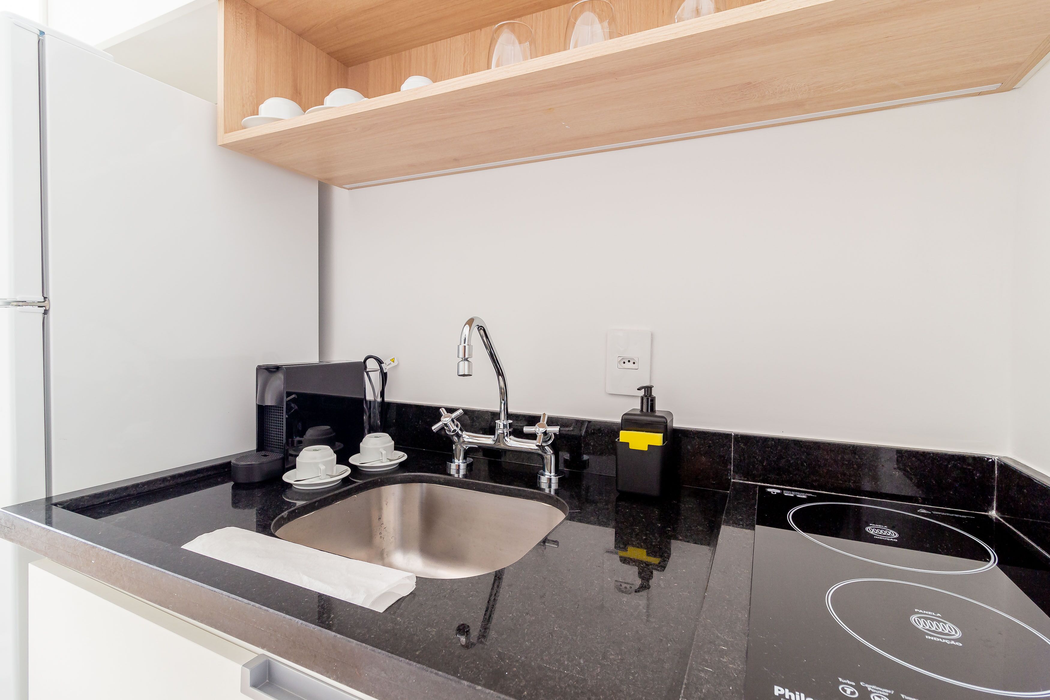 Una cocina moderna con un lavamanos de acero inoxidable, encimera negra y estantes de madera arriba.