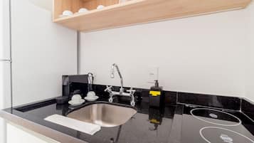 Una cocina moderna con un lavamanos de acero inoxidable, encimera negra y estantes de madera arriba.