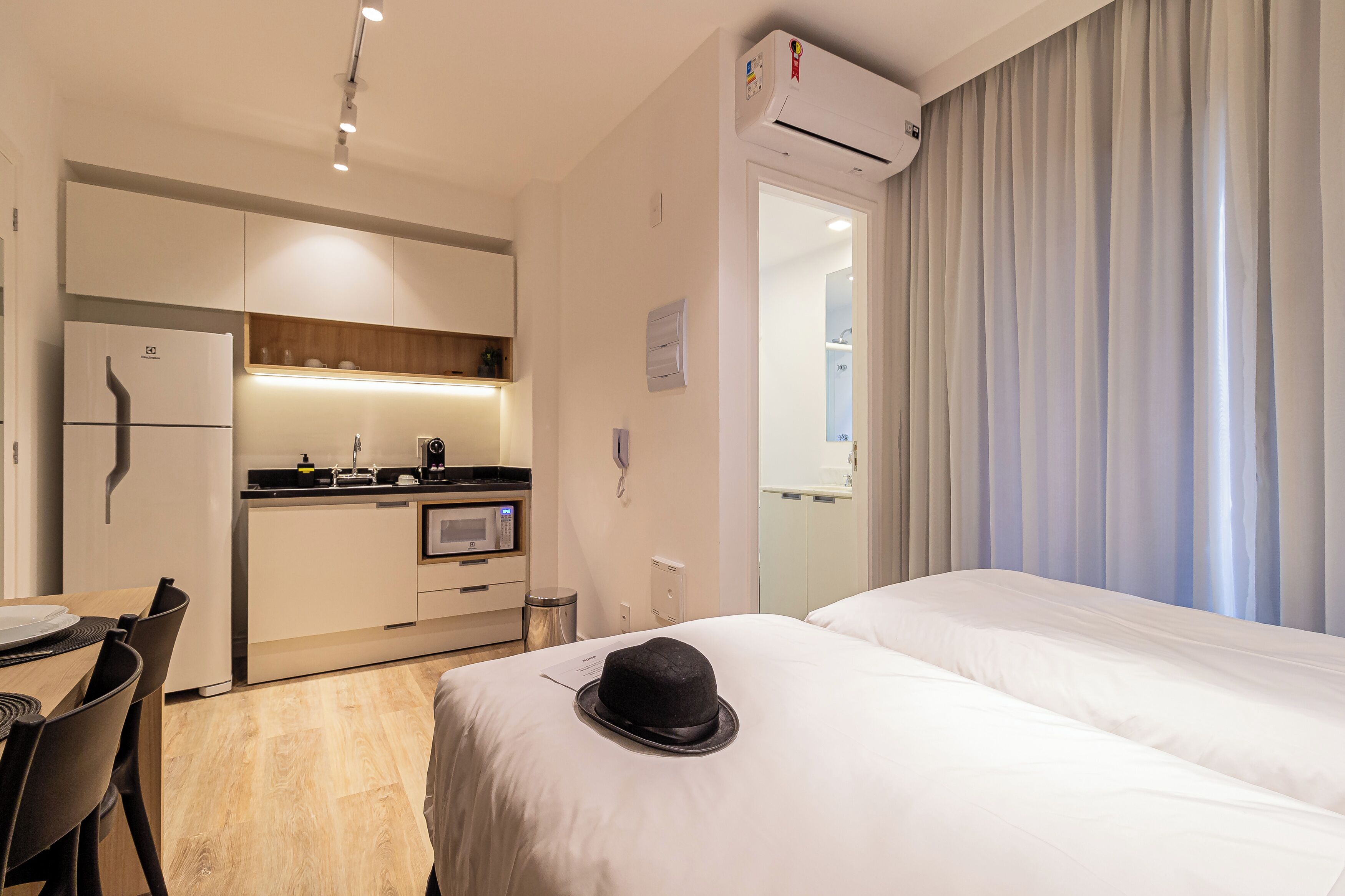 A hotel room with a bed, a dining table, a kitchenette, and a bathroom.