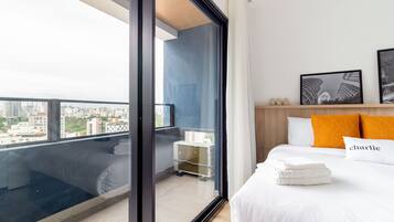 Una habitación de hotel moderna con un ventanal grande, una cama con ropa blanca, una almohada 'charlie' y cuadros enmarcados en la pared.