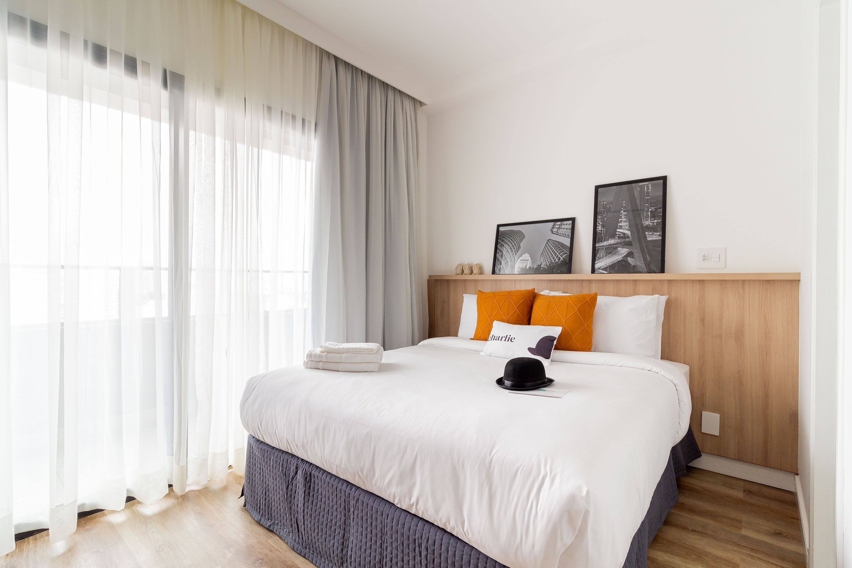 Cama bem arrumada com roupa de cama branca, um chapéu preto e duas fotos emolduradas na cabeceira.