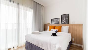 Cama bem arrumada com roupa de cama branca, um chapéu preto e duas fotos emolduradas na cabeceira.