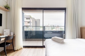 A hotel room with a bed, a desk, and a view of the city through a large sliding glass door. - Charlie Harmonia Vila Madalena (São Paulo)