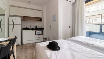 A hotel room with a bed, a dining table with chairs, a kitchenette, and a window with a view.