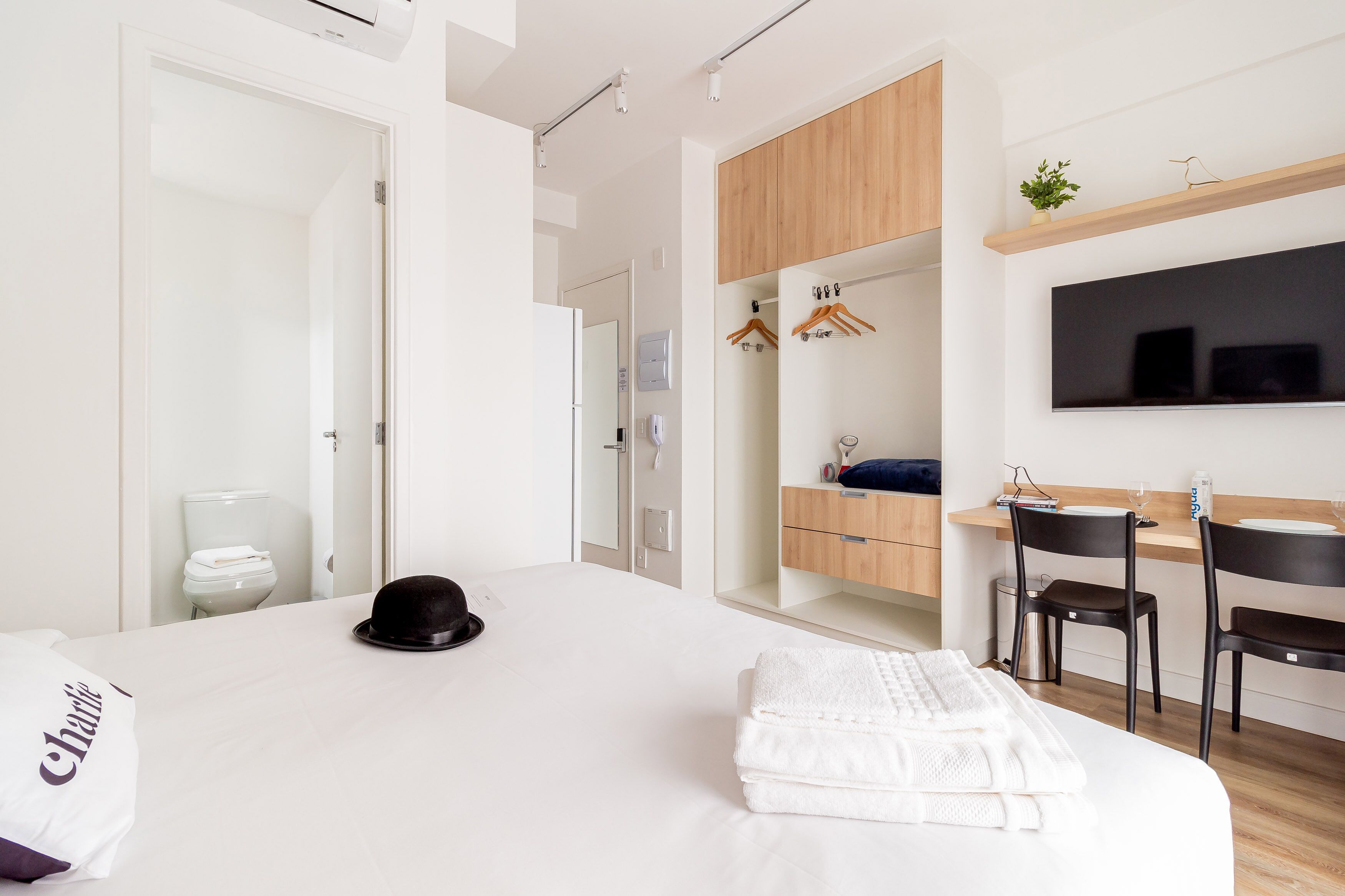 Une chambre d’hôtel moderne dotée d’un grand lit, d’un bureau avec une chaise, d’un téléviseur fixé au mur et d’une armoire en bois au-dessus du bureau.