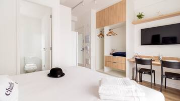 Une chambre d’hôtel moderne dotée d’un grand lit, d’un bureau avec une chaise, d’un téléviseur fixé au mur et d’une armoire en bois au-dessus du bureau.