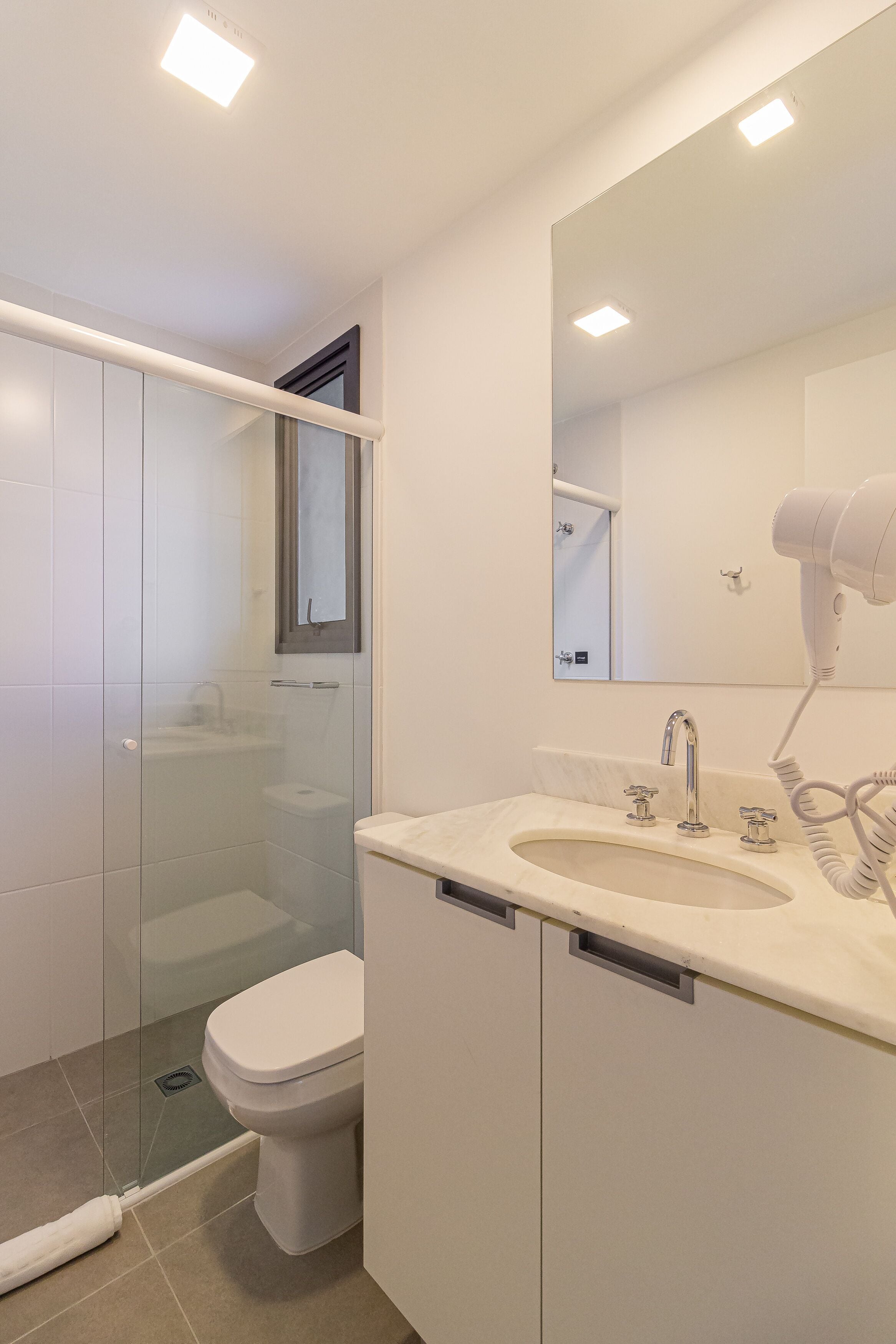 Un bagno moderno con box doccia in vetro, un water, un lavandino con specchio e un asciugacapelli sul ripiano.