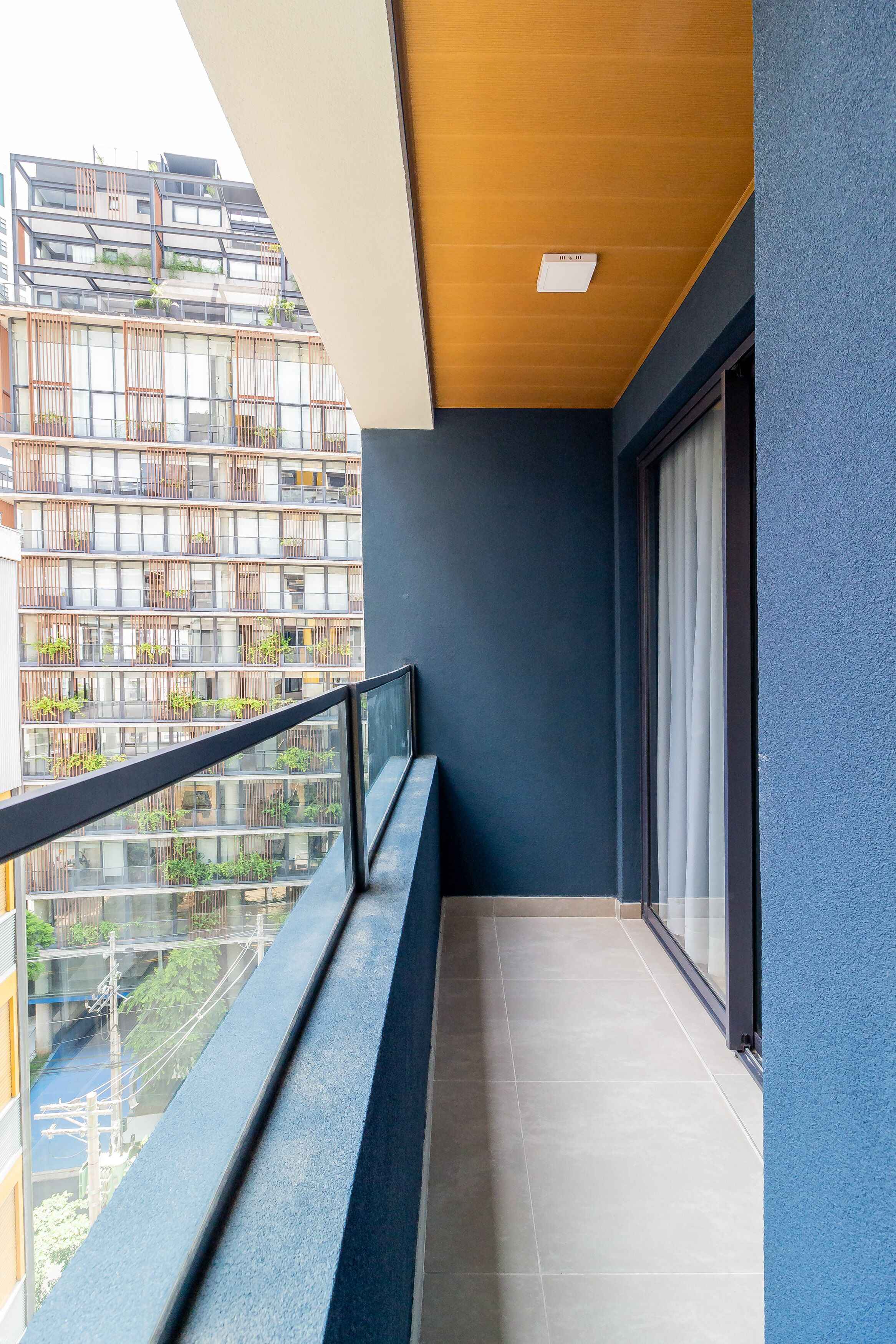 A balcony with a view of a modern building, a wooden ceiling, and a blue wall.