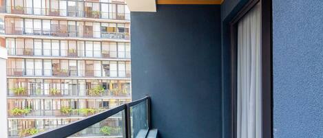 A balcony with a view of a modern building, a wooden ceiling, and a blue wall.