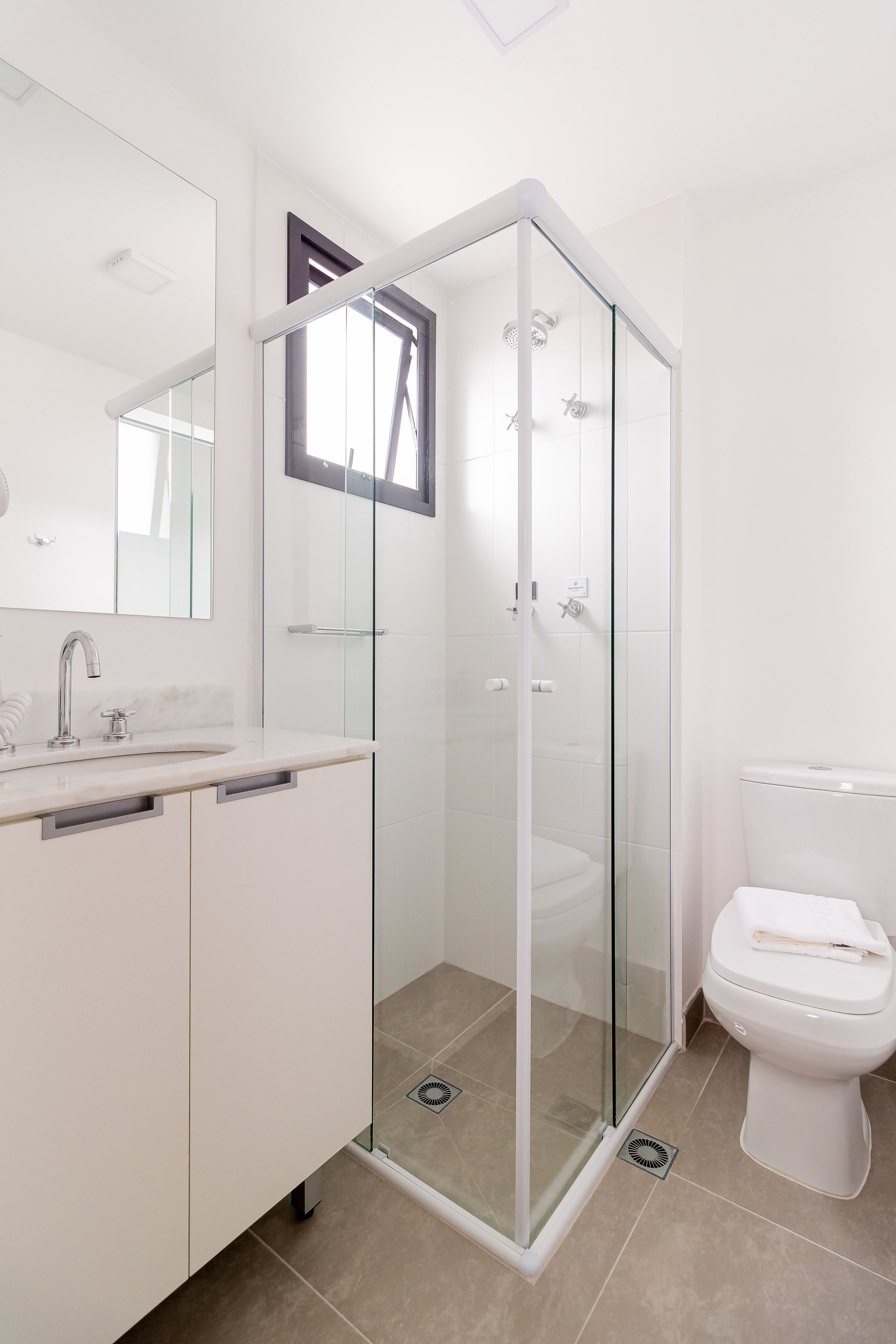 Un baño moderno con ducha de vidrio, un lavabo blanco con espejo y un inodoro.