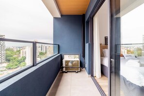 A narrow balcony with a view of a cityscape, a small air conditioning unit, and a bed with a pillow labeled "Charlie". - Charlie Harmonia Vila Madalena (São Paulo)