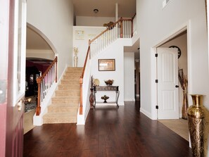 Un pasillo amplio con una escalera de madera, una consola decorativa y una puerta a la derecha.