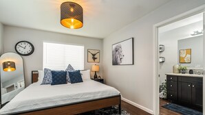 A bedroom with a bed, bedside lamps, a clock, and a window with blinds. - Tribune at Redlands, Arcade Hands (Redlands)