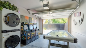 A garage with a pool table, arcade machines, a washing machine, and a ceiling-mounted projector. - Tribune at Redlands, Arcade Hands (Redlands)