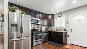 A modern kitchen with stainless steel appliances, dark wood cabinets, and a white door. - Tribune at Redlands, Arcade Hands (Redlands)