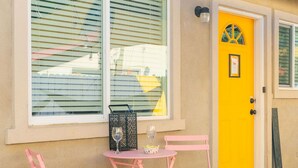 A building with a yellow door, a window with blinds, and a small table with chairs outside. - Tribune at Redlands, Arcade Hands (Redlands)
