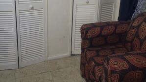 Una habitación con un sofá estampado, suelo de baldosas y armarios blancos con puertas a persiana.