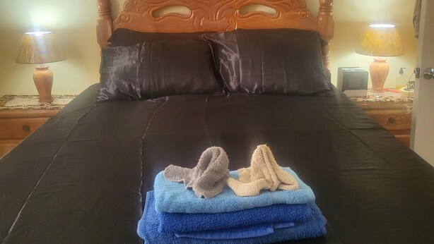 Una cama con cabecera de madera, dos mesitas de noche, una lámpara y un arreglo de toallas.