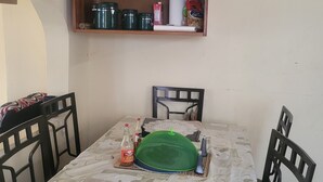 Un comedor con una mesa cubierta por un mantel, rodeada de sillas. Encima de la mesa, un aparador de madera con utensilios de cocina.