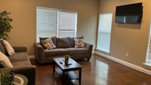A living room with a brown leather sofa, a coffee table, and a TV mounted on the wall. - Unit F (Moss Point)