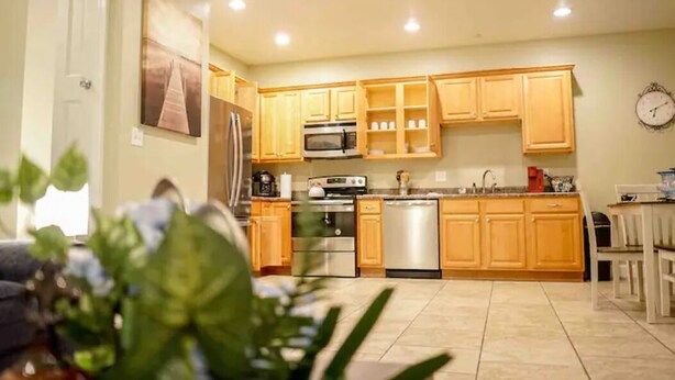 A modern kitchen with wooden cabinets, stainless steel appliances, and a dining area with a white table and chairs. - Unit F (Moss Point)