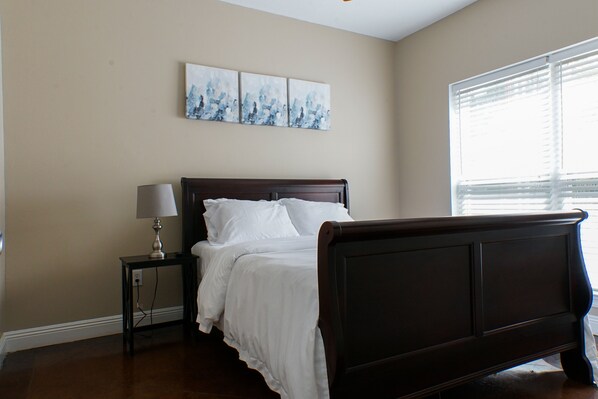 A bedroom with a bed, a nightstand, a lamp, and a window with blinds. - Unit F (Moss Point)