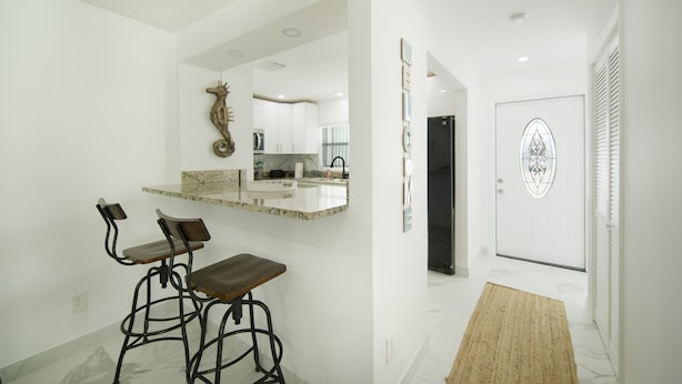 Une cuisine moderne dotée d’un plan de travail en marbre, de deux tabourets de bar et d’un miroir décoratif.