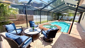 Ein überdachter Außenbereich mit Pool, Liegestühlen und einem Tisch.