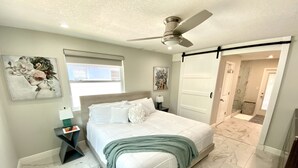 Ein Schlafzimmer mit einem Bett, einem Nachttisch, einem Deckenventilator und einer Tür zu einem Badezimmer.