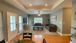 A spacious living room with a ceiling fan, a TV mounted on the wall, and a dining area with a table and chairs. - Unit G (Moss Point)