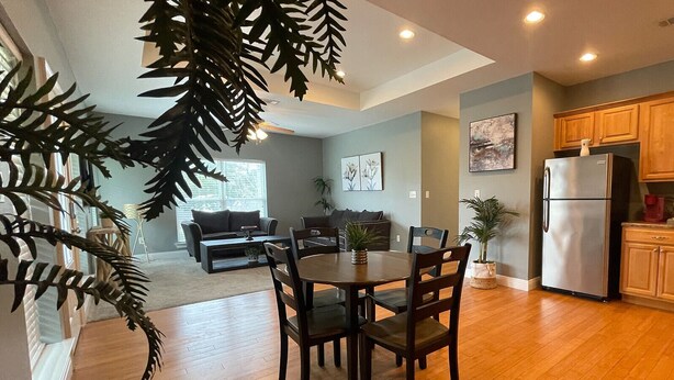 A modern kitchen with wooden cabinets, a stainless steel refrigerator, and a dining area with a wooden table and chairs. - Unit G (Moss Point)