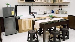 Una cucina compatta con frigorifero, piano cottura e pensili in legno. Si trova anche un tavolo da pranzo con quattro sgabelli.