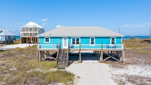 A two-story blue house with a balcony, a wooden deck, and a staircase leading to the deck.