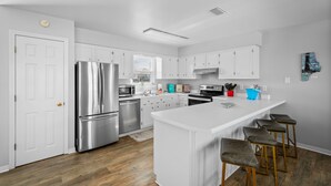 A modern kitchen with white cabinetry, stainless steel appliances, and a central island with stools.