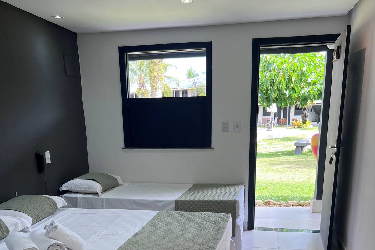 A hotel room with two beds, a window, and a door leading to a garden.
