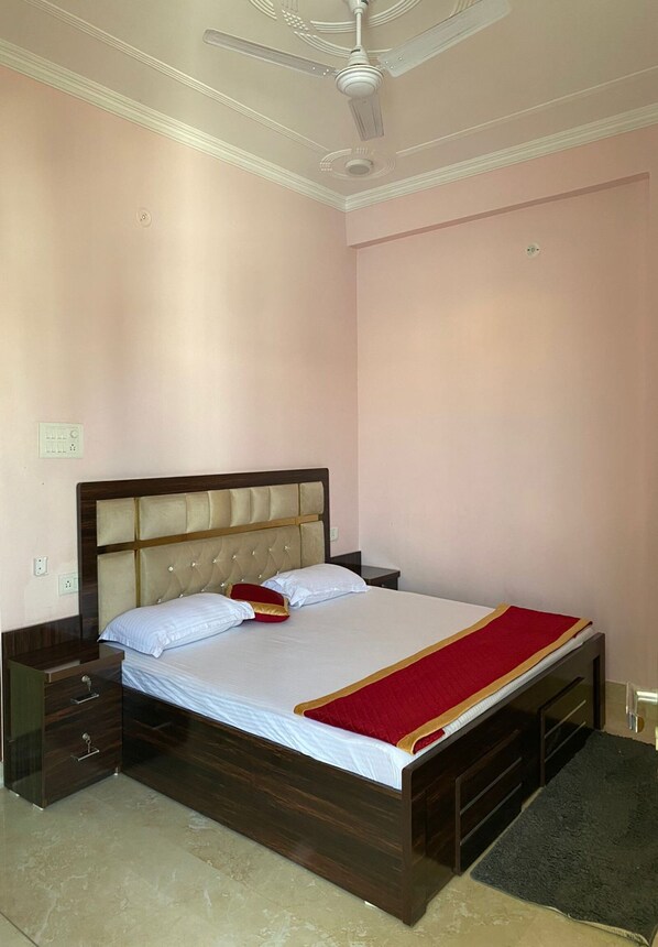 A bedroom with a wooden bed, a nightstand, a drawer unit, a ceiling fan, and a wall socket.