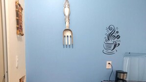 A small dining area with a wooden table and two chairs, a decorative wall piece, and a coffee machine.