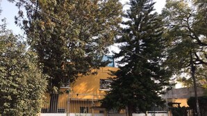 A residential building with a yellow facade, surrounded by trees and a gated entrance.