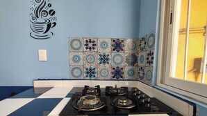 A kitchen with a gas stove, blue and white checkered floor, decorative tiles, and a window with a yellow wall outside.