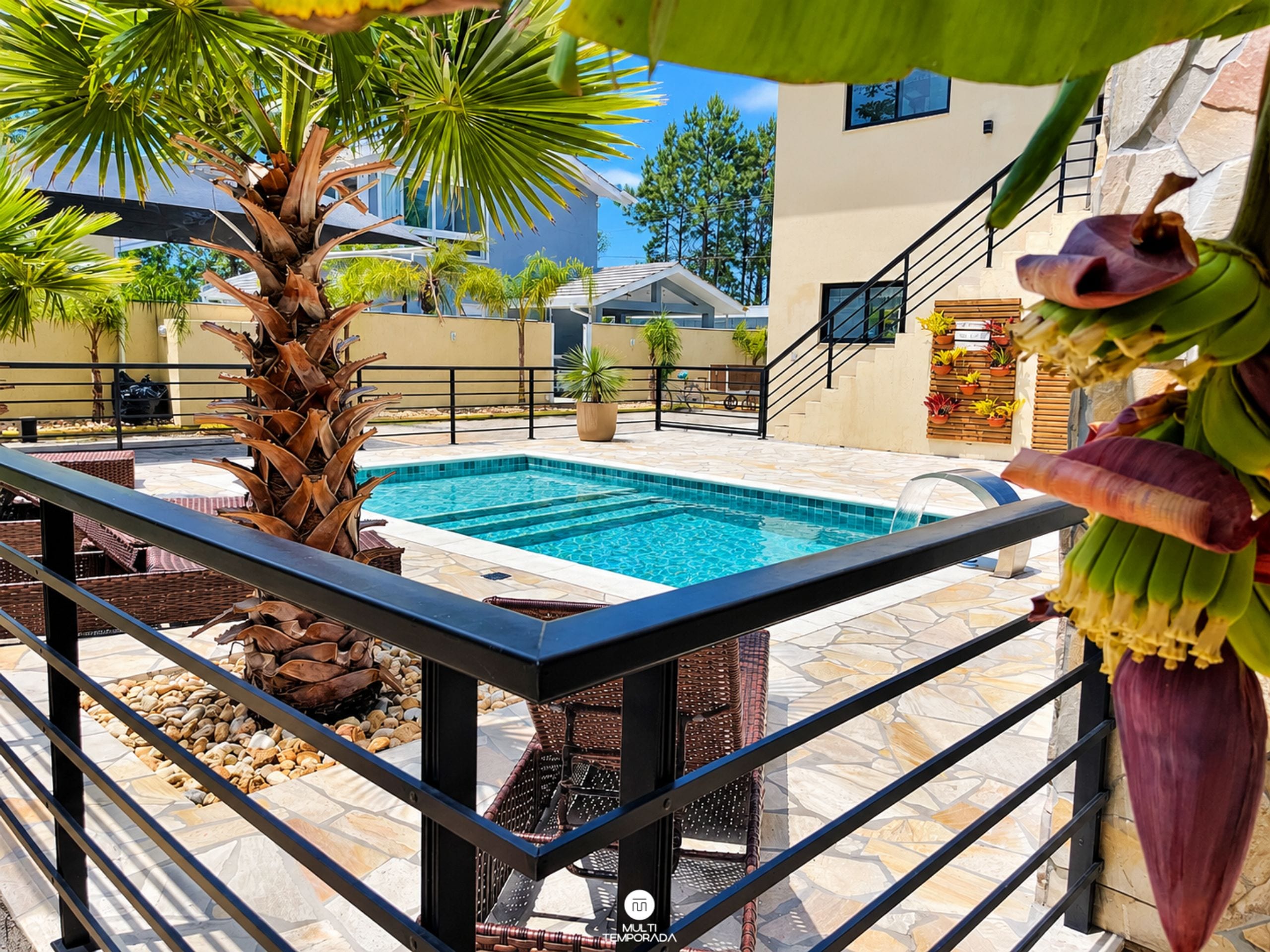 Una piscina con solárium empedrado, rodeada de palmeras y plantas en macetas.