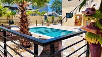 Una piscina con solárium empedrado, rodeada de palmeras y plantas en macetas.