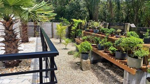 A rooftop garden with various potted plants, a stone-tiled floor, and a wooden railing. - Casa Privativa com Piscina na Ferrugem (Garopaba)