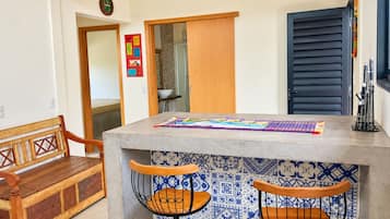 A kitchen with a wooden bench, two bar stools, a tiled backsplash, and a wooden door.