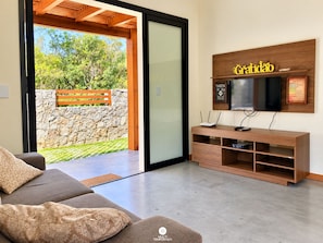A modern living room with a sofa, a TV mounted on a wooden wall, and a stone wall outside.
